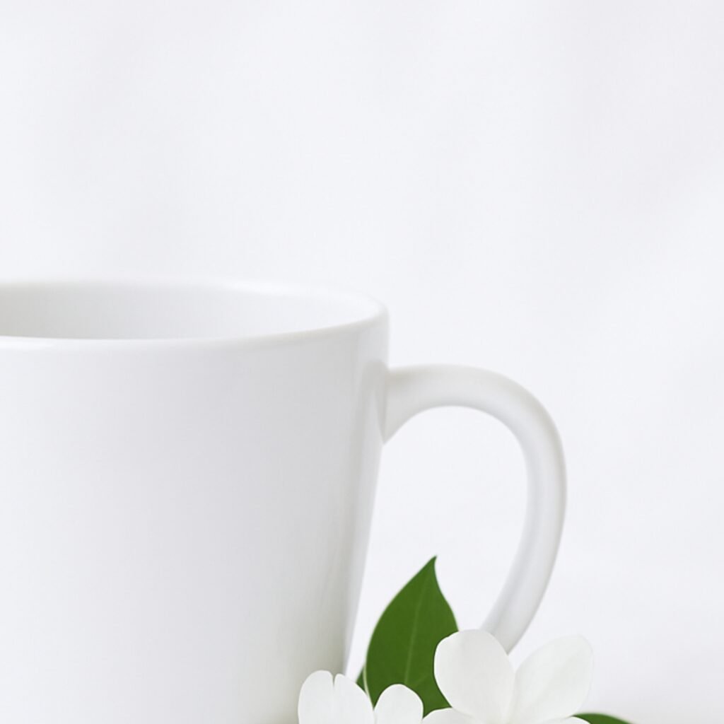 A stylish ceramic coffee cup for her, featuring an elegant floral design and a personalized name in a delicate script font, filled with steaming hot coffee, resting on a wooden coaster next to a small potted plant.