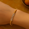Brother Rakhi 3 A close-up of a "Brother Rakhi" on a wrist, featuring "BROTHER" spelled out in sparkling, studded gold-toned letters, flanked by decorative golden beads on a subtle, light-colored thread, symbolizing deep sibling affection.