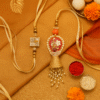 A "Designer Bhaiya Bhabhi Rakhi Set" featuring a brother's Rakhi with a sparkling square charm and a sister-in-law's Lumba Rakhi with an ornate red floral design, pearl border, and dangling bell tassel, all on elegant golden ribbons, symbolizing a rich and loving bond.