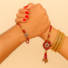 A "Traditional Floral Stone Bhaiya Bhabhi Rakhi Set" with a brother's Rakhi on a red thread featuring a round floral charm with red and white stones, and a matching Lumba Rakhi for the sister-in-law with a larger, ornate floral charm and red tassels, symbolizing love and prosperity.