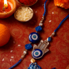 A "Bhaiya Bhabhi Evil Eye Rakhi Set" displayed on a golden plate, featuring one Rakhi with a simple blue evil eye bead for the brother and another (Lumba Rakhi) with a Hamsa hand charm and blue evil eye for the sister-in-law,