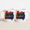 A white ceramic "Happy Birthday Mug" featuring a colorful, dripping paint-style "Happy Birthday" text, placed on a wooden desk with a blurred plant and papers in the background.