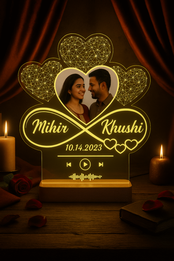 A personalized Acrylic Photo Lamp glowing warmly in a dim room, featuring a heart-shaped design with an etched photo of a couple, their names "Mihir" and "Khushi", a date "10.14.2023", and a music equalizer design, all mounted on a wooden base with candles and rose petals in the foreground.