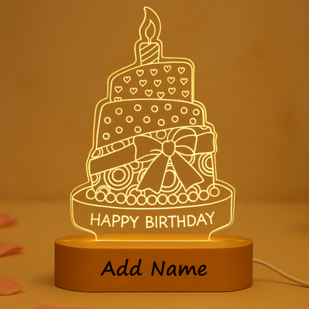 A glowing Personalized Birthday Acrylic LED Lamp shaped like a multi-tiered birthday cake with a candle on top, text "HAPPY BIRTHDAY," and a customizable "Add Name" section on its wooden base, set against a warm, blurred background.