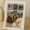 A white-framed Romantic Anniversary Photo Collage Frame featuring a main photo of a couple and smaller surrounding photos, with "Happy Anniversary" text, on a wooden table next to a vase