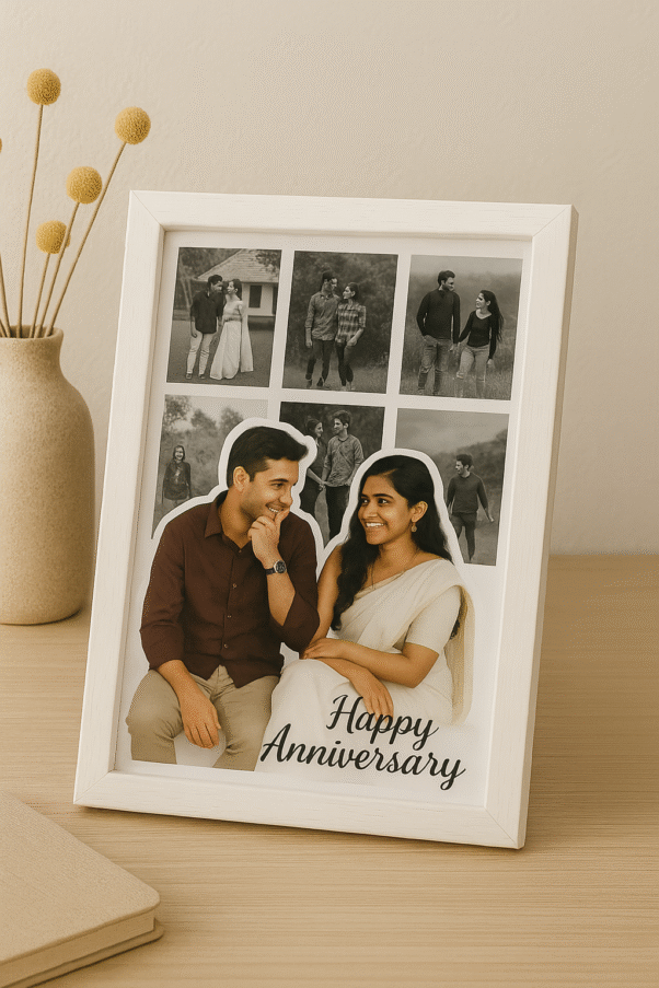 A white-framed Romantic Anniversary Photo Collage Frame featuring a main photo of a couple and smaller surrounding photos, with "Happy Anniversary" text, on a wooden table next to a vase