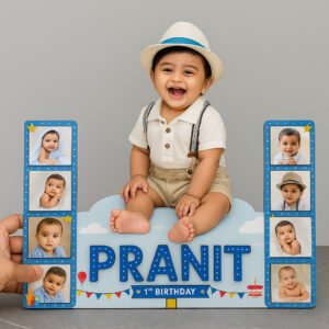A Wooden cutout photo for baby customized featuring a smiling baby (Pranit) sitting on a cloud-shaped base, flanked by two blue vertical panels with four small baby photos each, and text indicating "PRANIT 1st BIRTHDAY" with balloons and a cake icon.