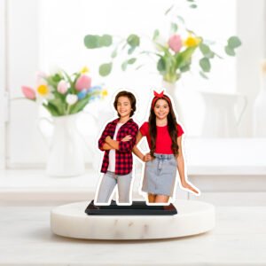 A "Brother Sister Personalized Caricature Stand" featuring a custom cutout of a young boy and girl smiling, designed for tabletop display, set against a bright indoor background with flowers.