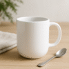 Custom White ceramic coffee mug with a rounded base, sitting on a wooden table next to a silver spoon and a folded beige cloth.