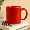 Custom red ceramic coffee mug sitting on a stack of books, with scattered coffee beans around it, in a studio setting.