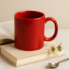 Custom red ceramic coffee mug sitting on a stack of books, with scattered coffee beans around it, in a studio setting.