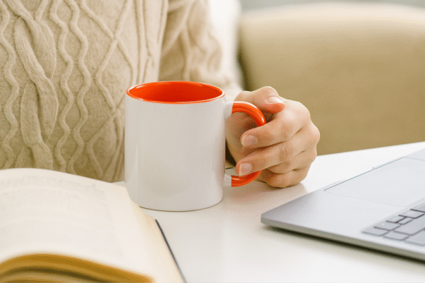 Orange and White Ceramic Coffee Mug a bright orange interior and handle, sitting on a table with an antique clock.