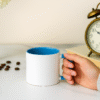 Bulk Ceramic Mugs Wholesale held by a hand on a table with a vintage alarm clock.