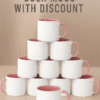 Custom Pink and white ceramic coffee mug with a pink interior and handle, sitting on a wooden table next to a vase with pink flowers, a stack of books, and scattered coffee beans.