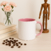 Custom Pink and white ceramic coffee mug with a pink interior and handle, sitting on a wooden table next to a vase with pink flowers, a stack of books, and scattered coffee beans.