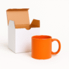 Personalize Full Orange Ceramic Coffee Mug the text "YOUR LOGO HERE" printed on the side, sitting on an office desk next to a laptop.
